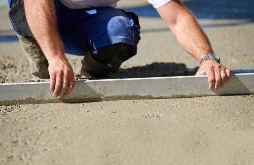 Worker screeding cement floor with screed